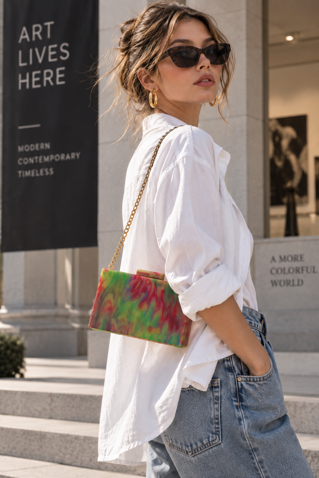 Young woman in white shirt and jeans wearing multicolor marbled acrylic box clutch with gold chain